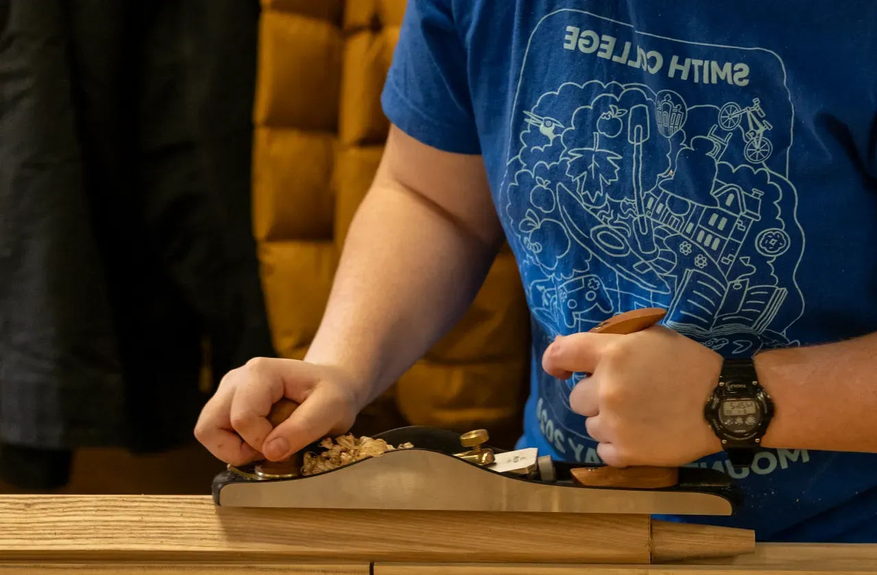  Elizabeth Rennert ‘25 in a blue 2024 Mountain Day shirt, pushes a Lie Neilson handplane across a block of wood